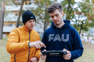 Zwei Studenten schauen auf eine Fernbedienung für eine Drohne und unterhalten sich angeregt.